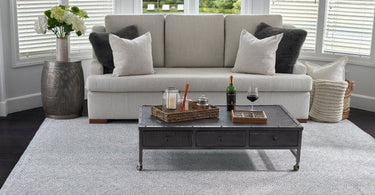 Light grey 8x10 wool rug under a sofa and dark coffee table in a bright living room