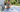 Woman scrubbing a blue and white striped polypropylene outdoor rug on a driveway with a soft brush, bucket of soapy water and garden hose