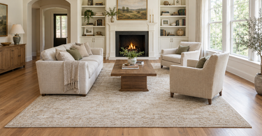 All-legs-on rug layout: sofa, two armchairs and coffee table fully on a large neutral 9x12 rug facing a fireplace