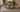 Rectangular walnut dining table with six chairs centered on an ivory and blue 8x10 wool rug, pulled-out chairs still fully on the rug
