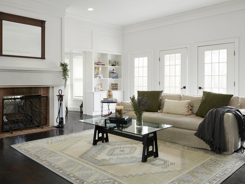 Living room with a light blue and cream Momeni Anatolia medallion rug under a glass coffee table, with a linen sofa and fireplace