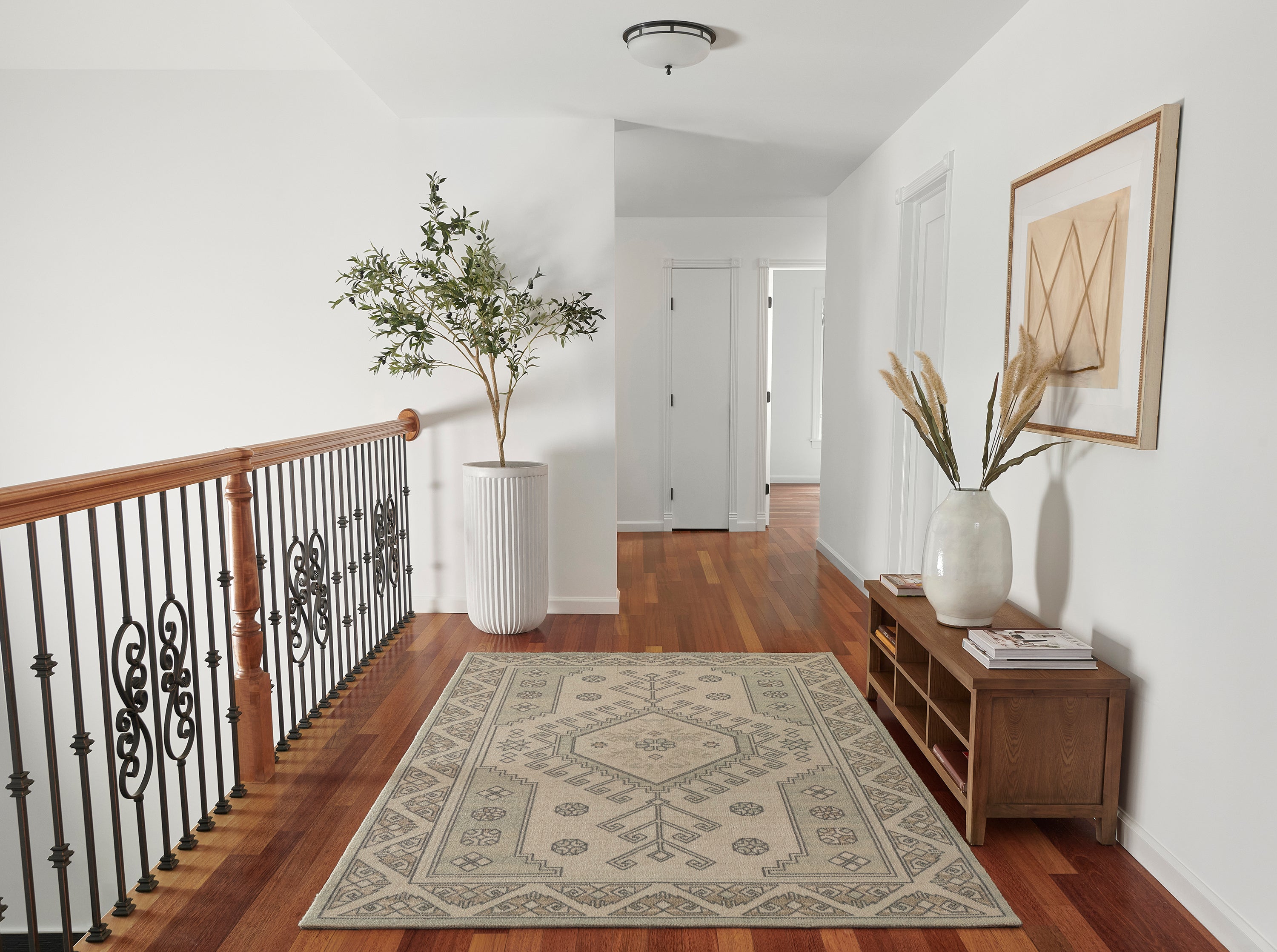 Sage and cream medallion rug on an upstairs landing beside a wood bench and a potted olive tree