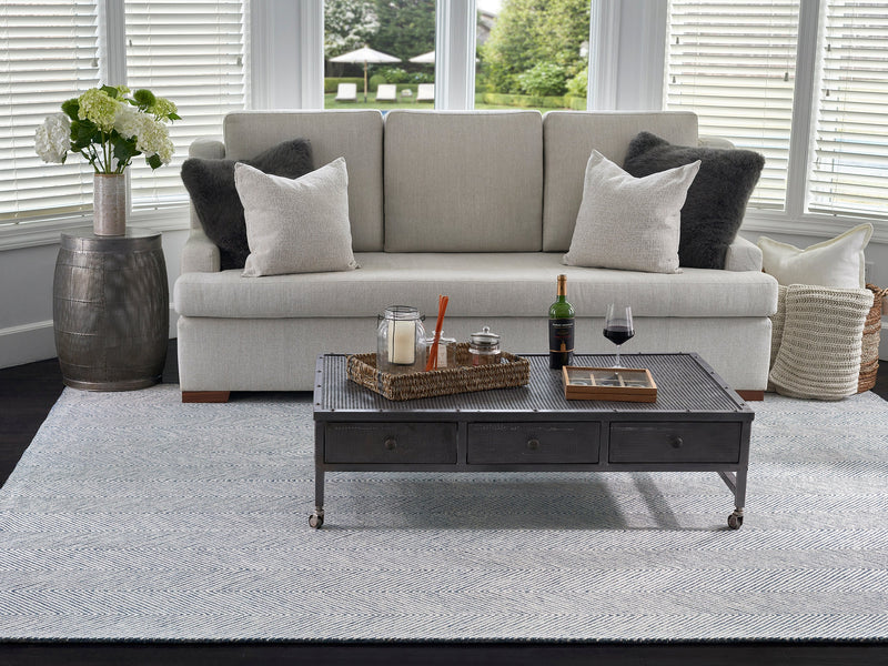 Light grey 8x10 wool rug under a sofa and dark coffee table in a bright living room