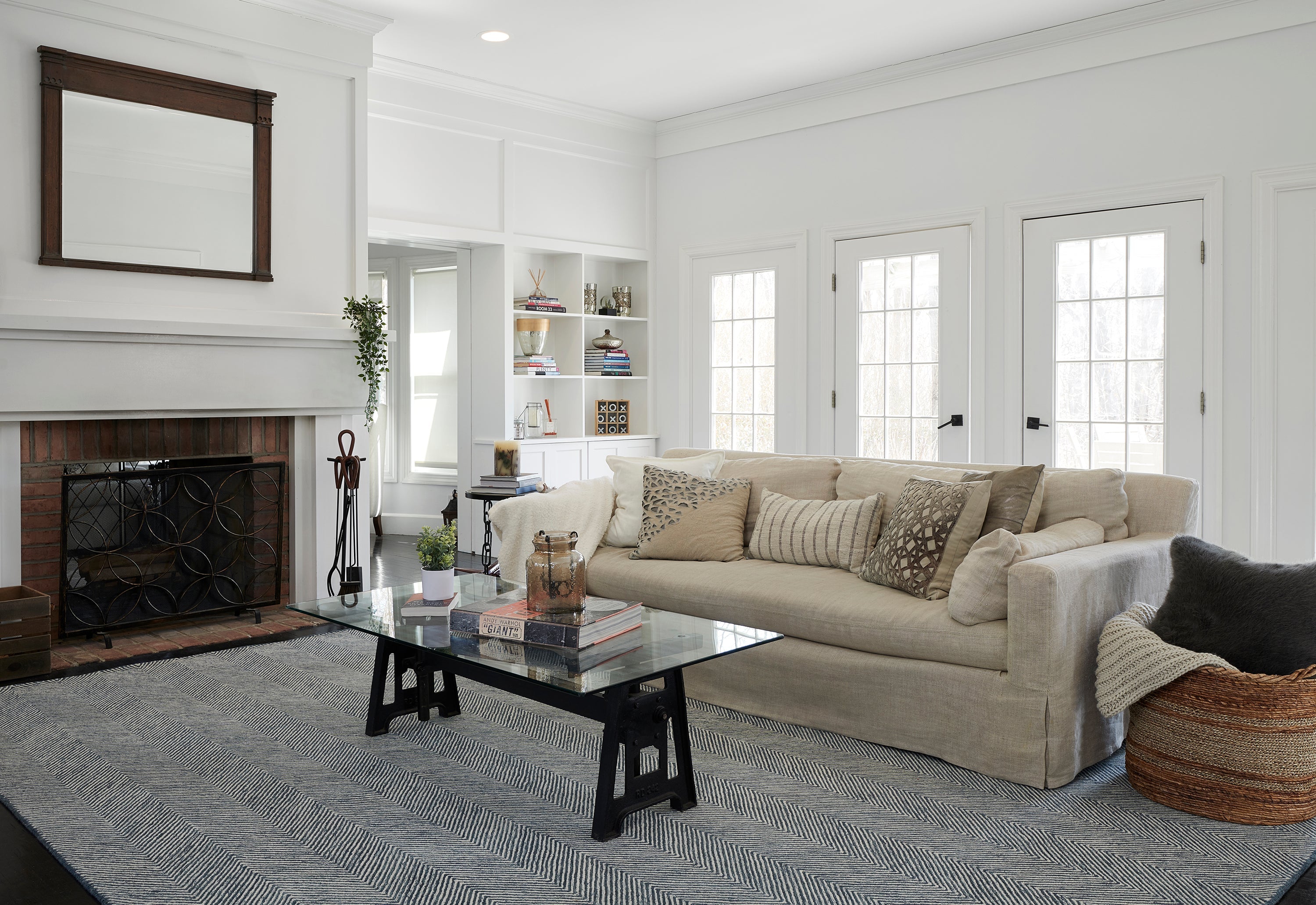 Grey hand-tufted wool rug under a glass coffee table and linen sofa in a bright living room with a fireplace