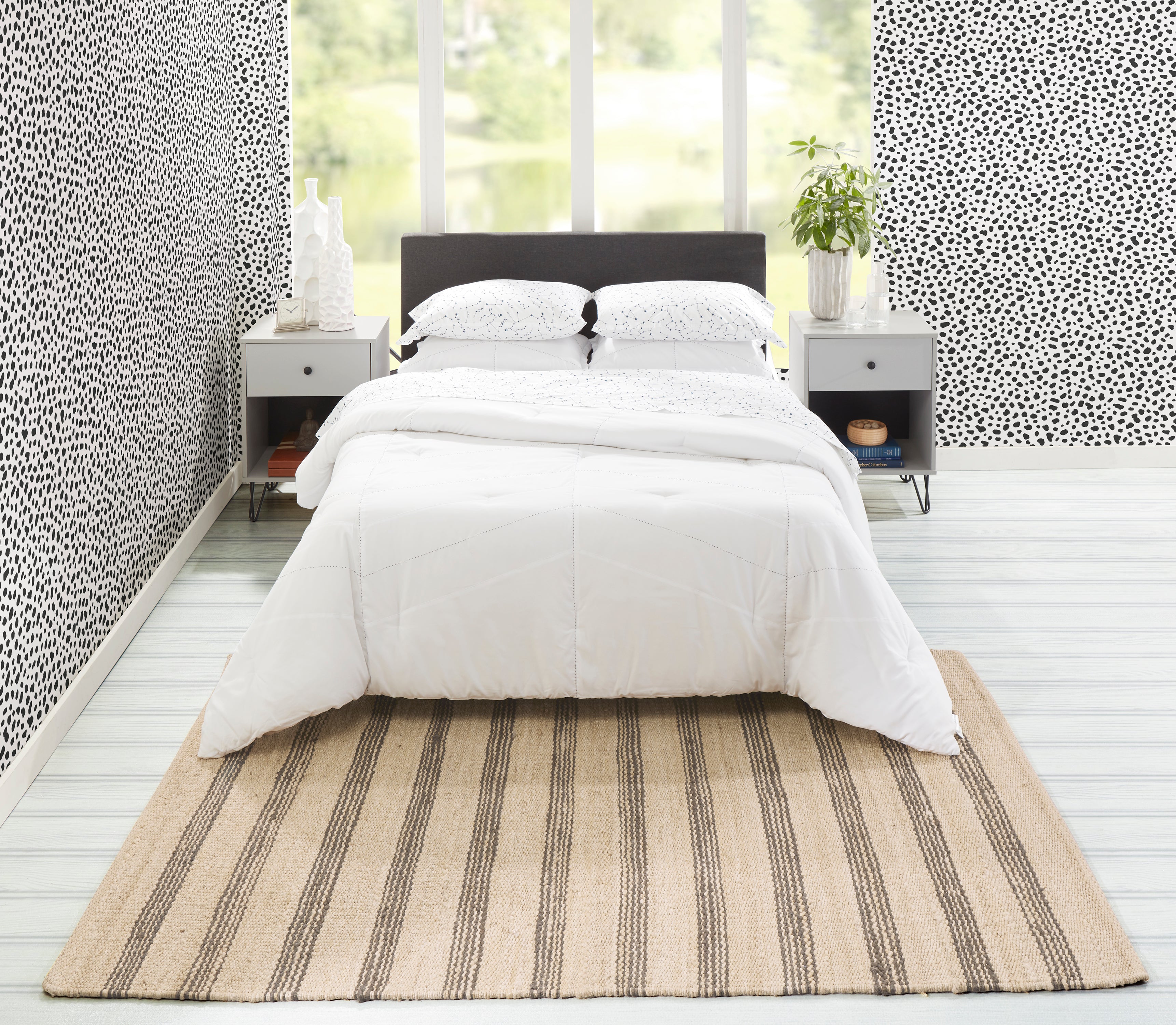 Striped hand-woven jute rug under a white bed in a bright bedroom