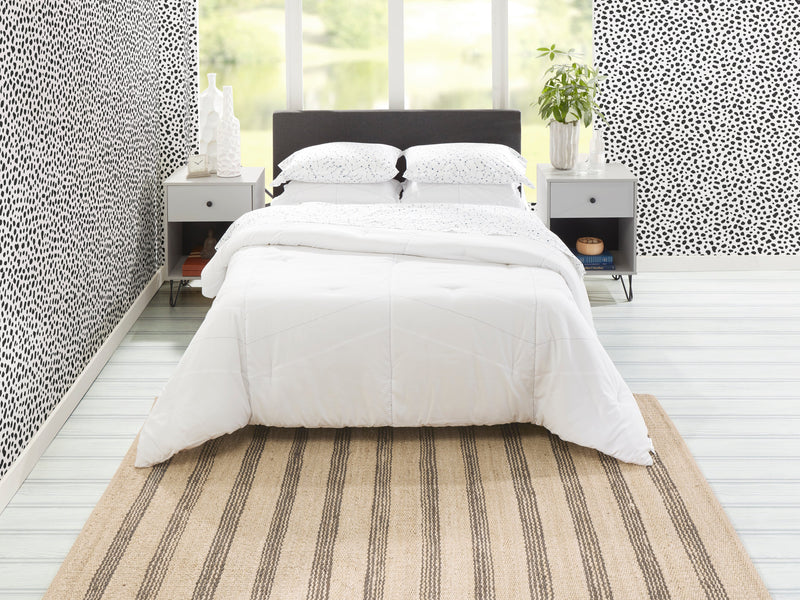 Striped hand-woven jute rug under a white bed in a bright bedroom