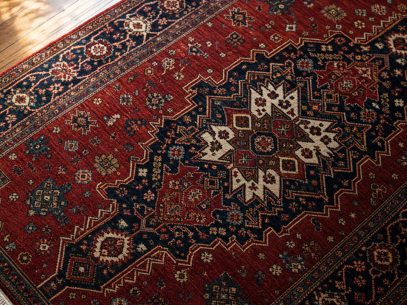 How to clean a Persian rug - close-up of a hand-knotted red and navy Persian rug on hardwood floor